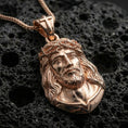 Load image into Gallery viewer, Rose gold plated religious Jesus pendant with expressive Christ portrait, crown of thorns, and sculpted bust silhouette resting on volcanic rock in an elegant close-up product presentation