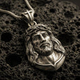Load image into Gallery viewer, Bronze Jesus Christ pendant with crown of thorns, sculpted sacred portrait, and detailed facial relief displayed on dark volcanic rock in a close-up luxury jewelry composition