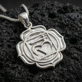 Load image into Gallery viewer, Polished silver chakra necklace with raised heart chakra emblem, angular sacred geometry, and layered lotus silhouette placed on textured volcanic rock in a premium studio product shot