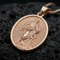 Load image into Gallery viewer, Rose gold plated Saint Paul necklace with haloed saint portrait, engraved devotional texture, and elegant oval silhouette resting on volcanic rock in an elegant close-up product presentation