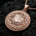 Load image into Gallery viewer, Rose gold plated spiritual medallion with centered Om motif, mandala-inspired patterning, and elegant round silhouette resting on volcanic rock in an elegant close-up product presentation