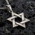 Load image into Gallery viewer, Oxidized Star of David pendant with interlocking geometric lines and open hexagram silhouette displayed on dark volcanic rock in a close-up luxury jewelry composition