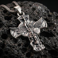 Load image into Gallery viewer, Oxidized Saint Michael pendant with winged archangel figure, Quis Ut Deus shield, and devil-slaying cross design displayed on dark volcanic rock in a close-up luxury jewelry composition