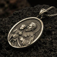 Load image into Gallery viewer, Bronze Saint Joseph pendant with Child Jesus, halo details, and oval devotional portrait displayed on dark volcanic rock in a close-up luxury jewelry composition