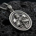 Load image into Gallery viewer, Oxidized Knight Templar pendant with crusader helmet, sword detail, and oval rotating medallion design displayed on dark volcanic rock in a close-up luxury jewelry composition