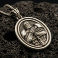 Load image into Gallery viewer, Bronze Knight Templar pendant with crusader helmet, sword detail, and oval rotating medallion design displayed on dark volcanic rock in a close-up luxury jewelry composition
