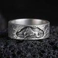 Load image into Gallery viewer, Oxidized sterling silver lion band ring on volcanic stone, macro close-up highlighting the carved lion relief, hammered texture, and deep shadow contrast.