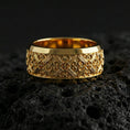 Load image into Gallery viewer, Gold plated cross scrollwork band ring on volcanic stone, luxury macro shot capturing warm gold tone across the decorative cross motifs and scroll accents.