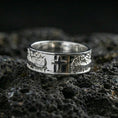 Load image into Gallery viewer, Polished silver cross band ring on volcanic stone, clean macro shot emphasizing bright reflective edges, smooth band finish, and sharp cross detail.