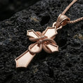 Load image into Gallery viewer, Rose gold plated gothic cross pendant with wrapped serpent motif, polished cross silhouette, and striking sculptural detail resting on volcanic rock in an elegant close-up product presentation