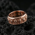 Load image into Gallery viewer, Skull motif sterling silver band ring on black volcanic stone, shown in a rose gold plated finish with a softer warm tone outlining each skull detail.