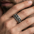 Load image into Gallery viewer, Skull motif sterling silver band ring worn on a finger, oxidized sterling silver look with high-contrast shadows emphasizing the gothic skull row.