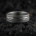 Load image into Gallery viewer, Sterling silver wave band ring on black volcanic stone, photographed with an oxidized patina that deepens the recessed swirl details and rope-edge borders.