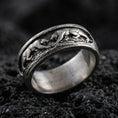 Load image into Gallery viewer, Sterling silver band ring photographed on black volcanic stone, featuring an oxidized finish that brings out the raised three-monkey relief and shadowed details.