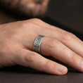 Load image into Gallery viewer, Oxidized sterling silver Greek key band worn on finger, meander pattern detail, natural lifestyle hand shot with shallow depth of field.