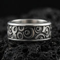 Load image into Gallery viewer, Oxidized sterling silver geometric spinner band ring on dark volcanic rock, raised circular pattern on rotating center, premium macro product shot.
