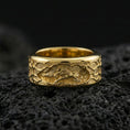 Load image into Gallery viewer, Gold plated spinning lion wedding band on volcanic rock, detailed lion engraving on rotating center with rugged pattern border, luxury jewelry product photography.