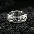 Load image into Gallery viewer, Polished silver wave filigree fidget spinner ring on black volcanic stone, crisp swirling scroll relief with smooth comfort edges, centered close-up studio lighting.