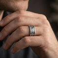 Load image into Gallery viewer, Oxidized sterling silver mountain range band worn on finger, rugged skyline engraving detail, natural lifestyle hand shot with shallow depth of field.