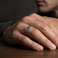 Load image into Gallery viewer, Oxidized sterling silver floral garden band worn on finger, raised daisy blossoms and leaf scroll detail, natural lifestyle hand shot with shallow depth of field.
