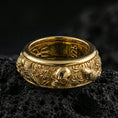 Load image into Gallery viewer, Gold plated skull and koi spinner band ring on volcanic rock, detailed skull relief with carp, clouds, and wave pattern on rotating band, luxury jewelry product photography.