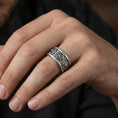 Load image into Gallery viewer, Oxidized sterling silver lion medallion band worn on finger, lion head relief panels and cross motif detail, natural lifestyle hand shot with shallow depth of field.