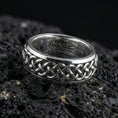 Load image into Gallery viewer, Polished silver braided Celtic knot ring on dark volcanic stone, bright reflective weave links with clean edges, premium close-up jewelry photography.