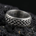 Load image into Gallery viewer, Oxidized sterling silver Celtic knot band ring on black volcanic rock, raised interwoven braid pattern with deep shadowed recesses, crisp macro product shot.