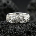 Load image into Gallery viewer, Polished silver wolf and deer engraved band ring on dark volcanic stone, crisp sculpted details with clean reflective highlights, premium close-up.