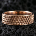 Load image into Gallery viewer, Rose gold plated woven-grid band ring on black volcanic stone, soft warm highlights defining the raised grid texture, luxury product shot.