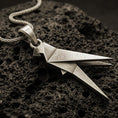 Load image into Gallery viewer, Bronze origami parrot pendant with geometric folded bird form and sleek angular silhouette displayed on dark volcanic rock in a close-up luxury jewelry composition