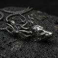 Load image into Gallery viewer, Oxidized stag pendant with detailed deer head, branching antlers, and realistic wildlife silhouette displayed on dark volcanic rock in a close-up luxury jewelry composition