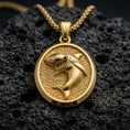 Load image into Gallery viewer, Gold plated shark pendant with bold shark figure, open jaws, and classic oval medallion form showcased on black volcanic rock in a refined macro jewelry image