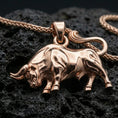 Load image into Gallery viewer, Rose gold plated bull necklace with muscular animal relief, detailed horn shape, and elegant Taurus-inspired silhouette resting on volcanic rock in an elegant close-up product presentation