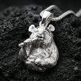 Load image into Gallery viewer, Polished silver panda necklace with sculpted bear face, realistic fur relief, and bamboo detail placed on textured volcanic rock in a premium studio product shot