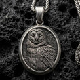 Load image into Gallery viewer, Oxidized owl pendant with detailed feather engraving, oval medallion frame, and calm nocturnal bird silhouette displayed on dark volcanic rock in a close-up luxury jewelry composition