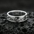 Load image into Gallery viewer, Polished silver floral engraved wedding band on volcanic rock, bright smooth edges with crisp scrolling leaf motifs in macro detail.