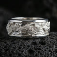 Load image into Gallery viewer, 925 silver wolf pack spinning band on black volcanic stone, polished silver edges framing the detailed wolf engraving.