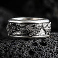 Load image into Gallery viewer, Sterling silver wolf spinner ring photographed on volcanic rock with oxidized contrast highlighting the wolf heads and forest scenery.