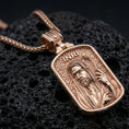 Load image into Gallery viewer, Rose gold plated devotional Jesus pendant with framed portrait, engraved background, and INRI inscription resting on volcanic rock in an elegant close-up product presentation
