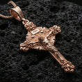 Load image into Gallery viewer, Rose gold plated crucifix pendant with detailed Christ figure, baroque cross silhouette, and engraved ornamentation resting on volcanic rock in an elegant close-up product presentation