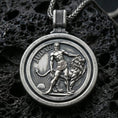 Load image into Gallery viewer, Oxidized Lion of Judah rotating pendant with a circular medallion design, lion figure, and Judah inscription displayed on dark volcanic rock in a close-up luxury jewelry composition