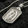 Load image into Gallery viewer, Polished silver Virgin of Guadalupe pendant with radiant halo detail, rounded rectangular frame, and engraved background placed on textured volcanic rock in a premium studio product shot