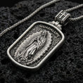Load image into Gallery viewer, Oxidized Our Lady of Guadalupe pendant with framed devotional figure and Guadalupe inscription displayed on dark volcanic rock in a close-up luxury jewelry composition