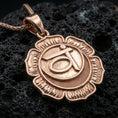 Load image into Gallery viewer, Rose gold plated spiritual chakra pendant with floral lotus frame, circular disc detail, and symbolic throat chakra motif resting on volcanic rock in an elegant close-up product presentation