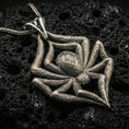 Load image into Gallery viewer, Oxidized spider pendant with textured legs, sculpted body relief, and bold arachnid silhouette displayed on dark volcanic rock in a close-up luxury jewelry composition