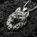 Load image into Gallery viewer, Oxidized polygonal wolf pendant with faceted geometric wolf head, angular sculpted planes, and bold spirit animal silhouette displayed on dark volcanic rock in a close-up luxury jewelry composition