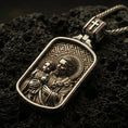 Load image into Gallery viewer, Bronze Saint Joseph pendant with Child Jesus, halo details, and framed devotional portrait displayed on dark volcanic rock in a close-up luxury jewelry composition