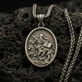 Load image into Gallery viewer, Bronze saint medallion pendant with a seated bearded figure, lion detail, and open scripture relief displayed on dark volcanic rock in a close-up luxury jewelry composition