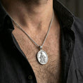 Load image into Gallery viewer, Polished silver Saint Rochus pendant with halo and dog relief worn on the neck in a close lifestyle frame, highlighting the detailed saint figure and sacred symbolism